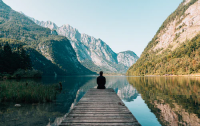man sitting on dock by mountains