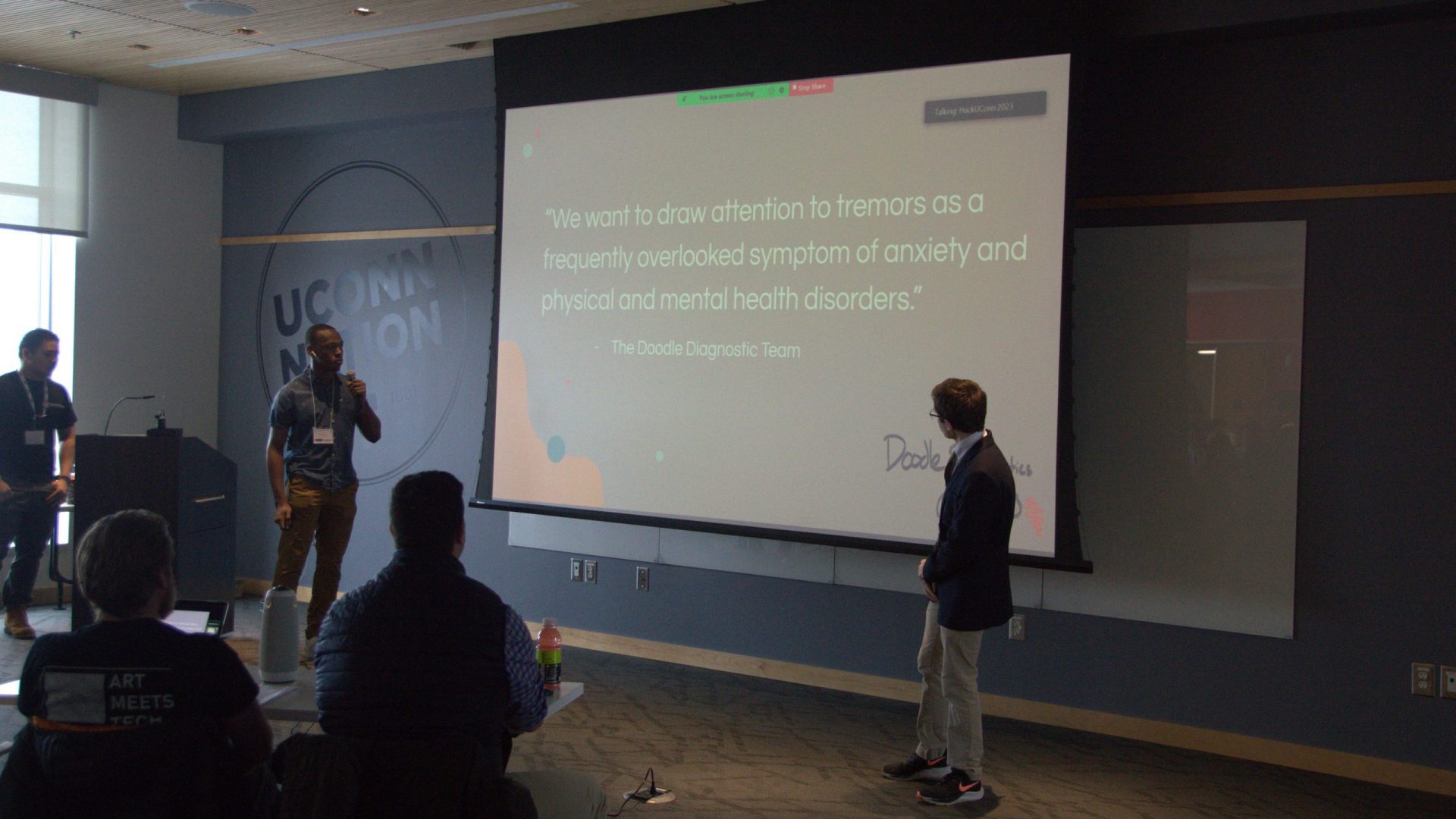 Two students stand at in front of their presentation slides at HackUConn 2023